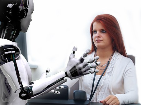 Woman in white coat sits at desk opposite a prototype AI robot that has the physical structure similar to a human